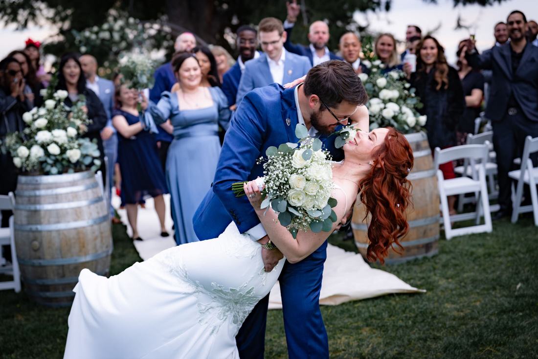 Groom dipping bride for a kiss as guests cheer